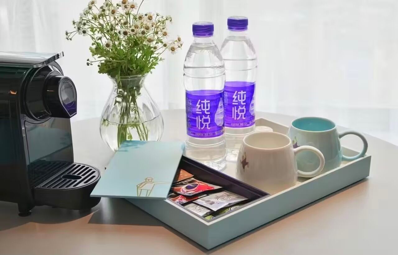 A coffee maker, two water bottles, a mug, a tray with a card, and a vase with flowers on a table.