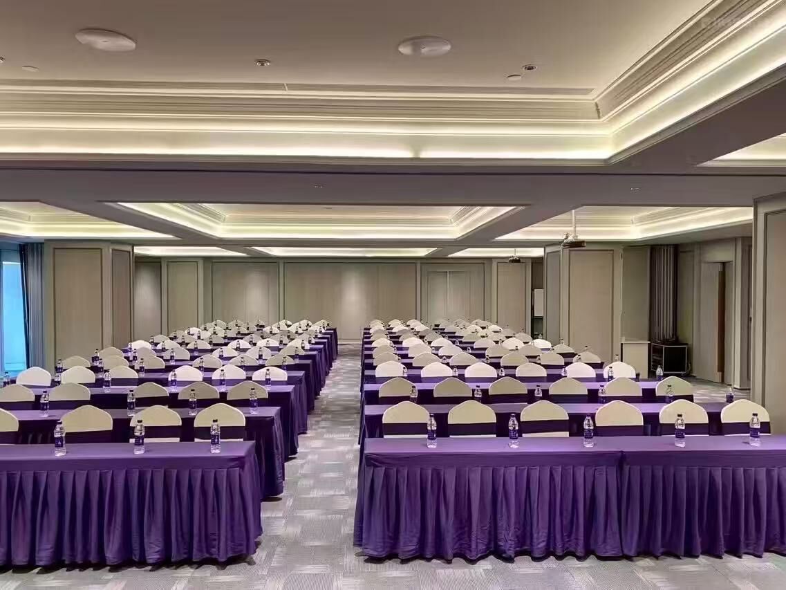 Un salón de conferencias con mesas y sillas dispuestas en filas, equipado con botellas de agua.