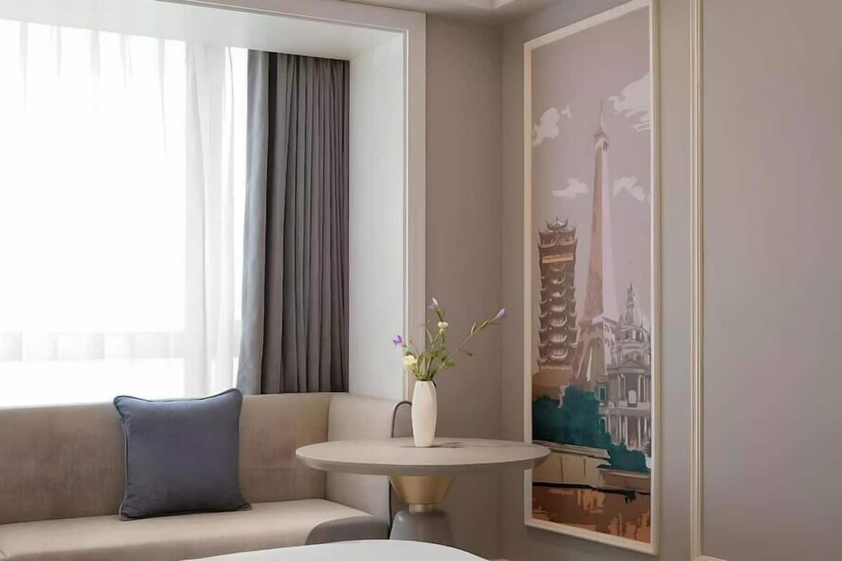 A hotel room with a sofa, a small round table, a vase with flowers, and a wall mural.