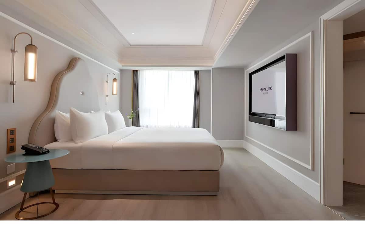 A modern hotel room with a large bed, a round table, a TV, and a view of the city.