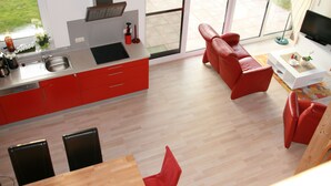 Uma cozinha moderna com armários vermelhos, uma área de refeições com mesa e cadeiras de madeira, e um sofá vermelho.