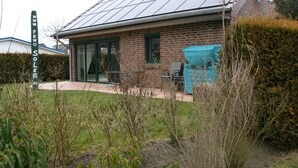 Uma casa com telhado solar, fachada de tijolos e área de estar coberta ao ar livre.