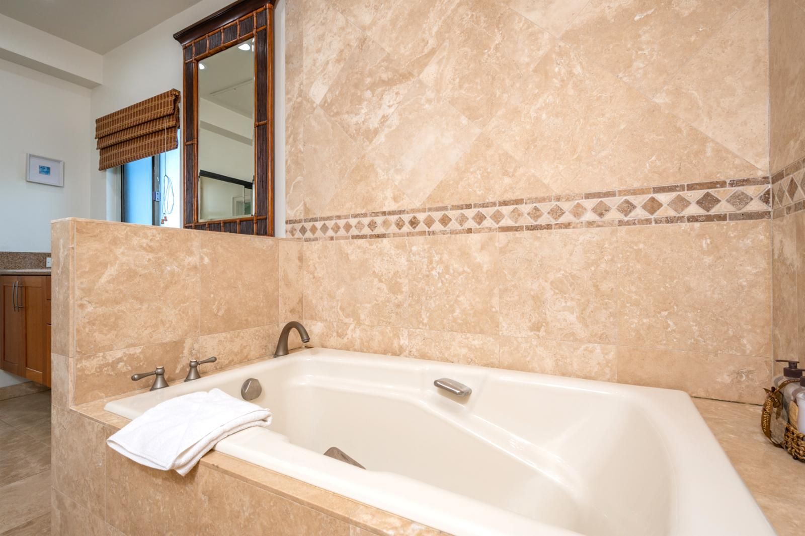 A bathroom with a large bathtub, a mirror, and a window with blinds.