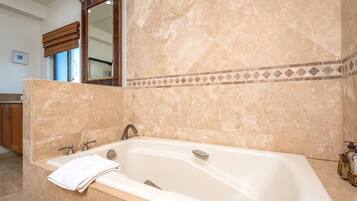 A bathroom with a large bathtub, a mirror, and a window with blinds.