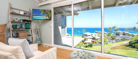 Uma sala de estar ampla com uma grande porta de vidro deslizante que dá para uma varanda com vista para o oceano e os edifícios do resort.