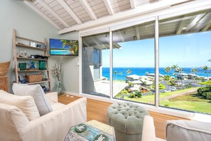 Ein großzügiges Wohnzimmer mit einem großen Schiebeglastür, die auf einen Balkon mit Blick aufs Meer und die Hotelgebäude führt.