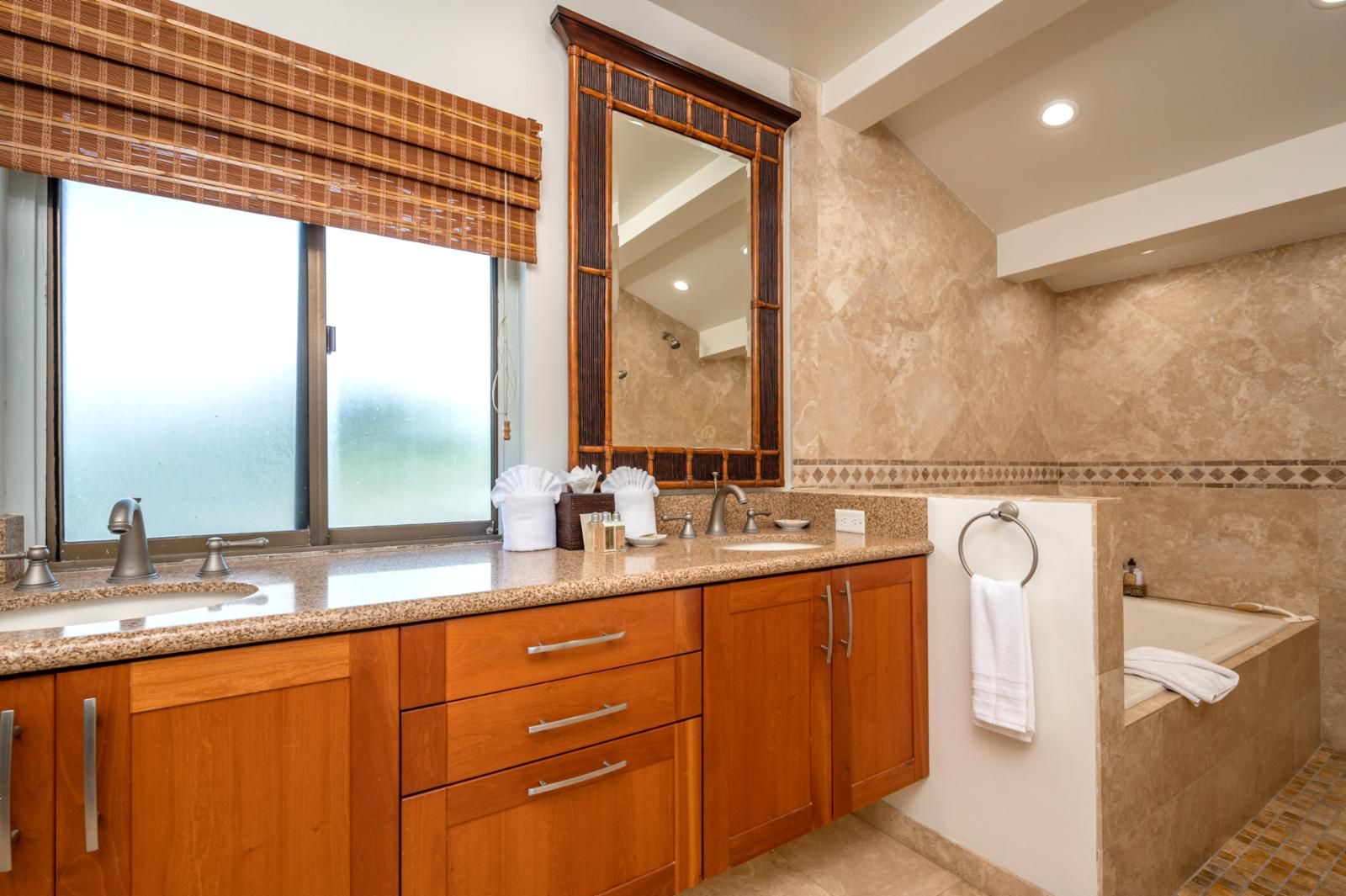 Un bagno moderno con un piano in granito, mobili in legno, uno specchio grande e una vasca da bagno.