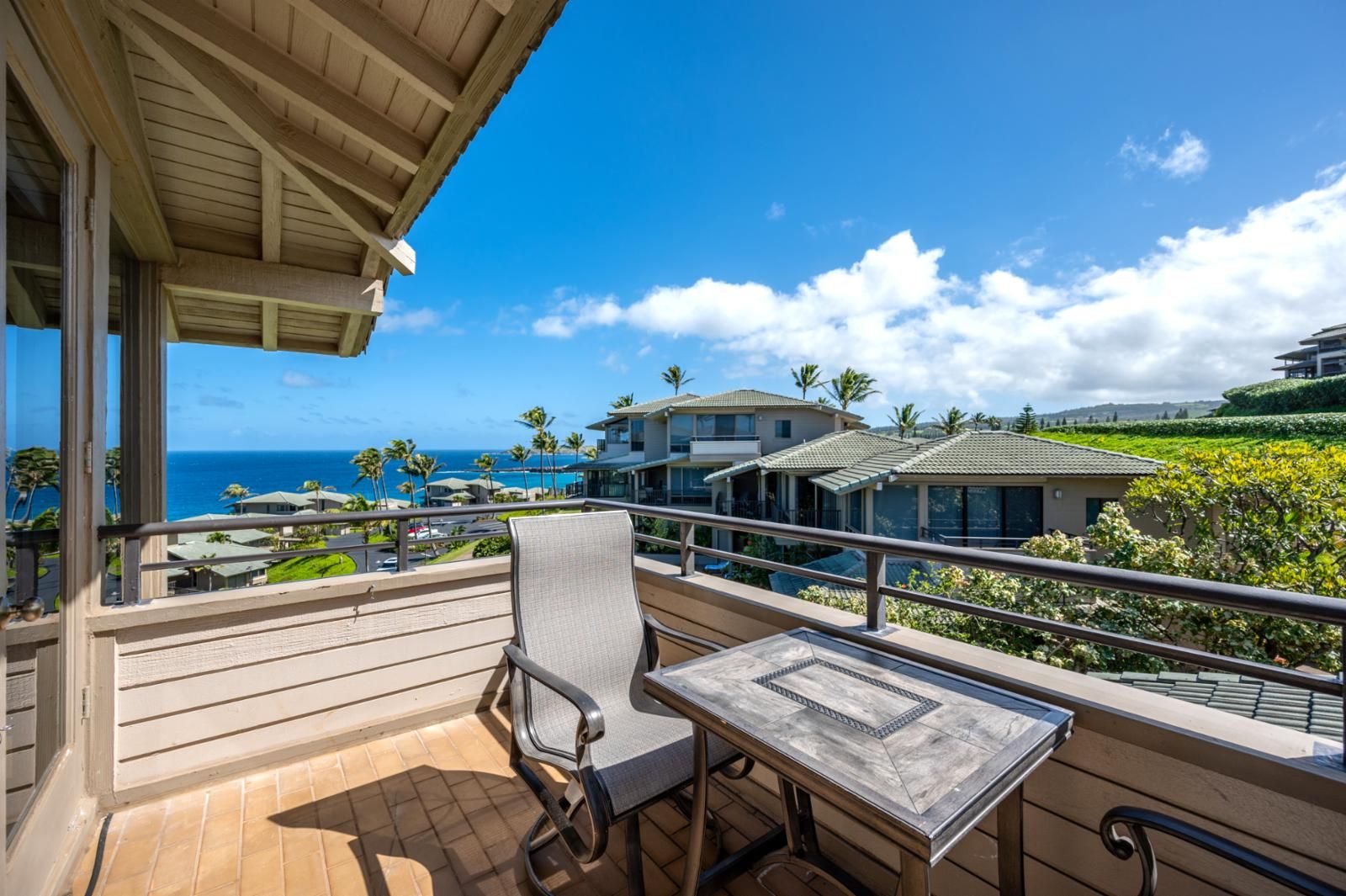 A balcony with a table and chairs, overlooking a coastal area with houses and palm trees.