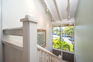 A staircase with a white railing, a framed picture on the wall, and a view of a parking lot with cars and greenery outside.