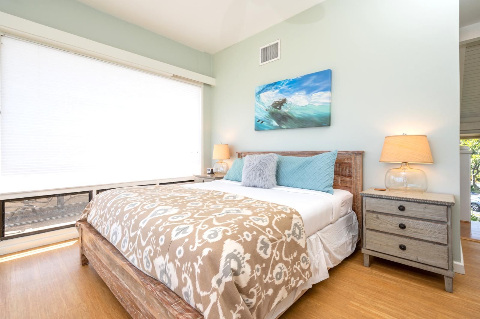 Een slaapkamer met een groot bed, twee nachtkastjes met lampen, een raam met jaloezieën en een schilderij aan de muur.