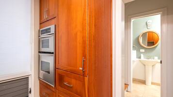 A kitchen with wooden cabinets, a built-in oven, and a view into the adjacent bathroom with a sink and mirror.