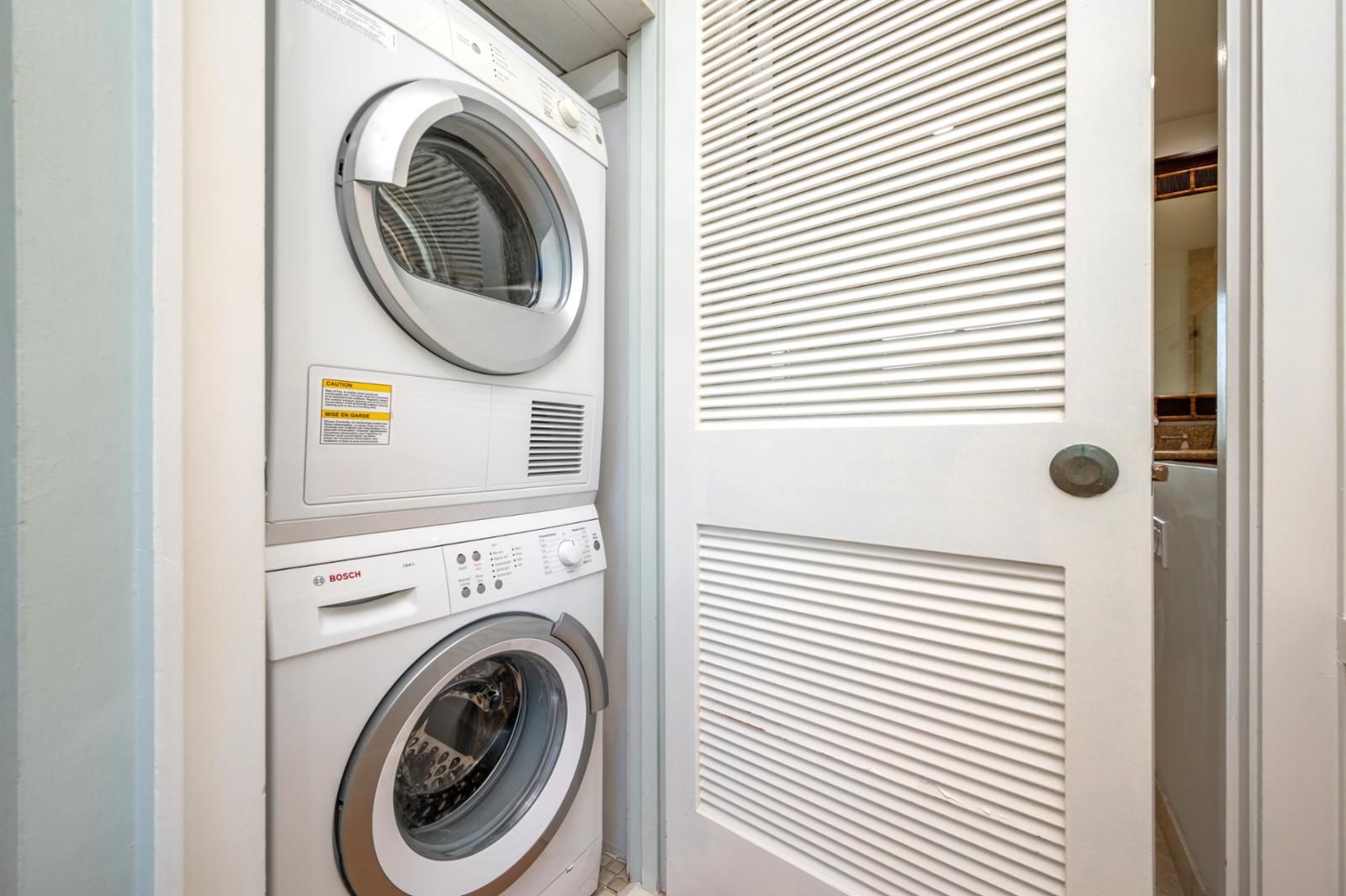 Een gestapelde wasmachine en droger in een wasserij, met een deur naar een gang.