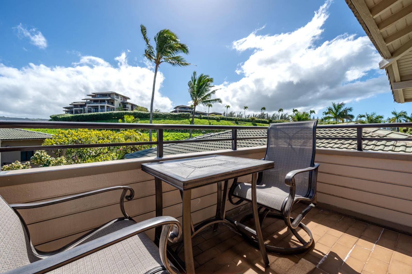 A balcony with a table and chairs, overlooking a landscaped area with palm trees and a building in the background.