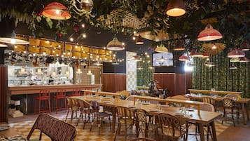 Un restaurante con mesas y sillas de madera, lámparas colgantes y una zona de bar.