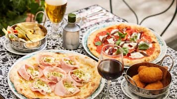 A table with two pizzas, a glass of beer, a bottle of olive oil, and a bowl of croquettes.