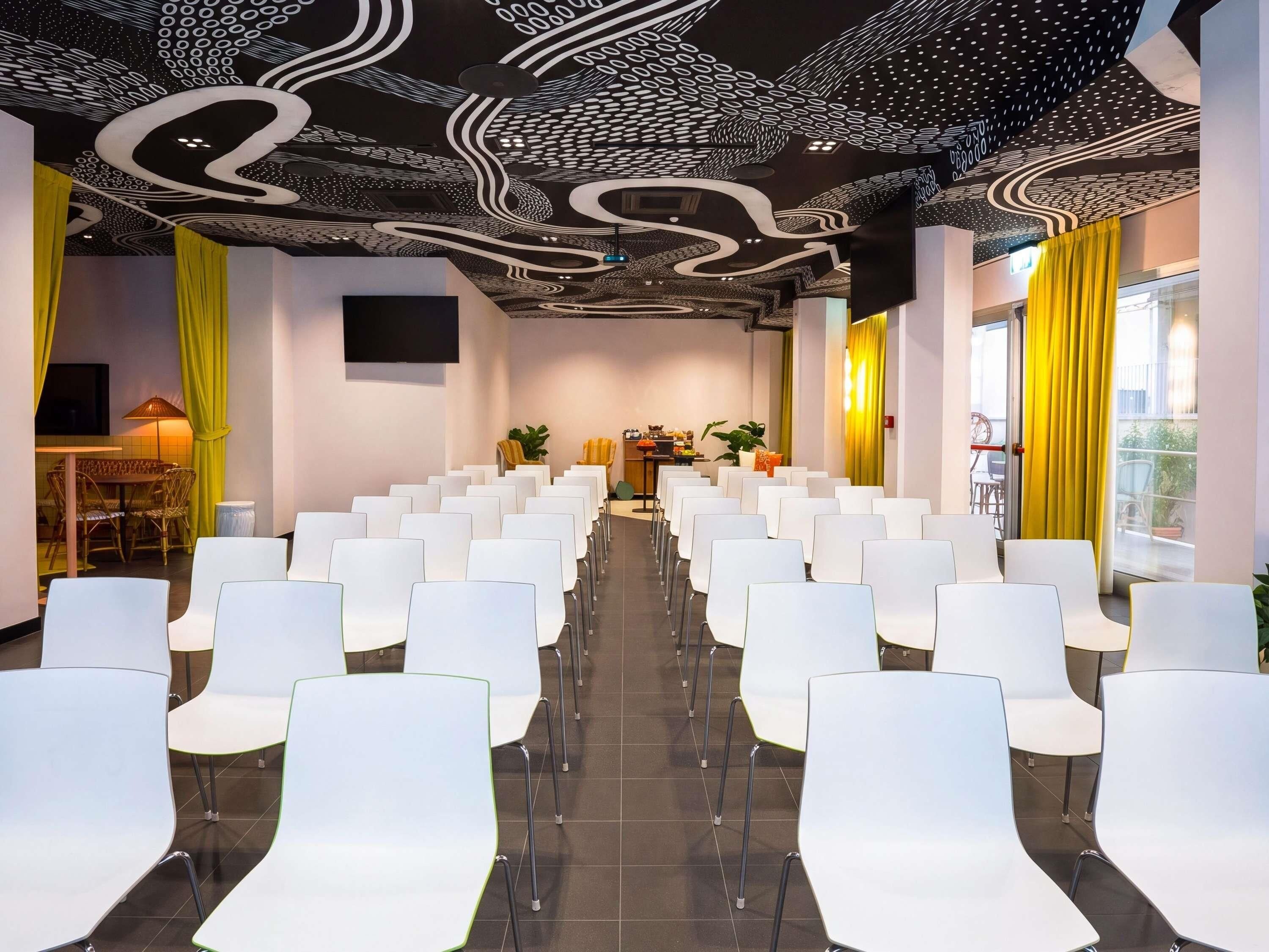 A conference room with rows of white chairs, a stage with a podium, and a ceiling with a unique black and white pattern.