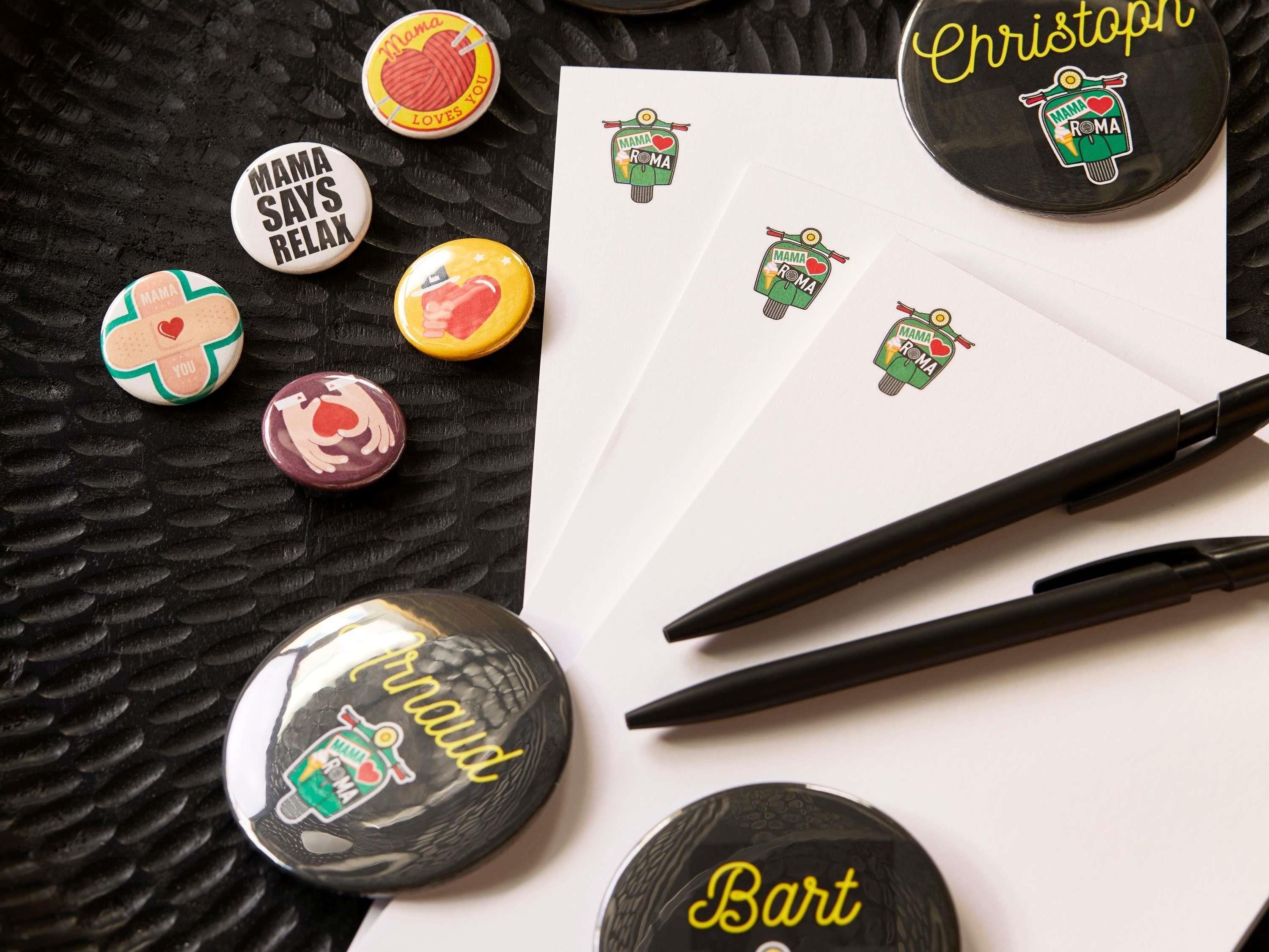 A collection of buttons with various designs and text, a pen, and some papers.