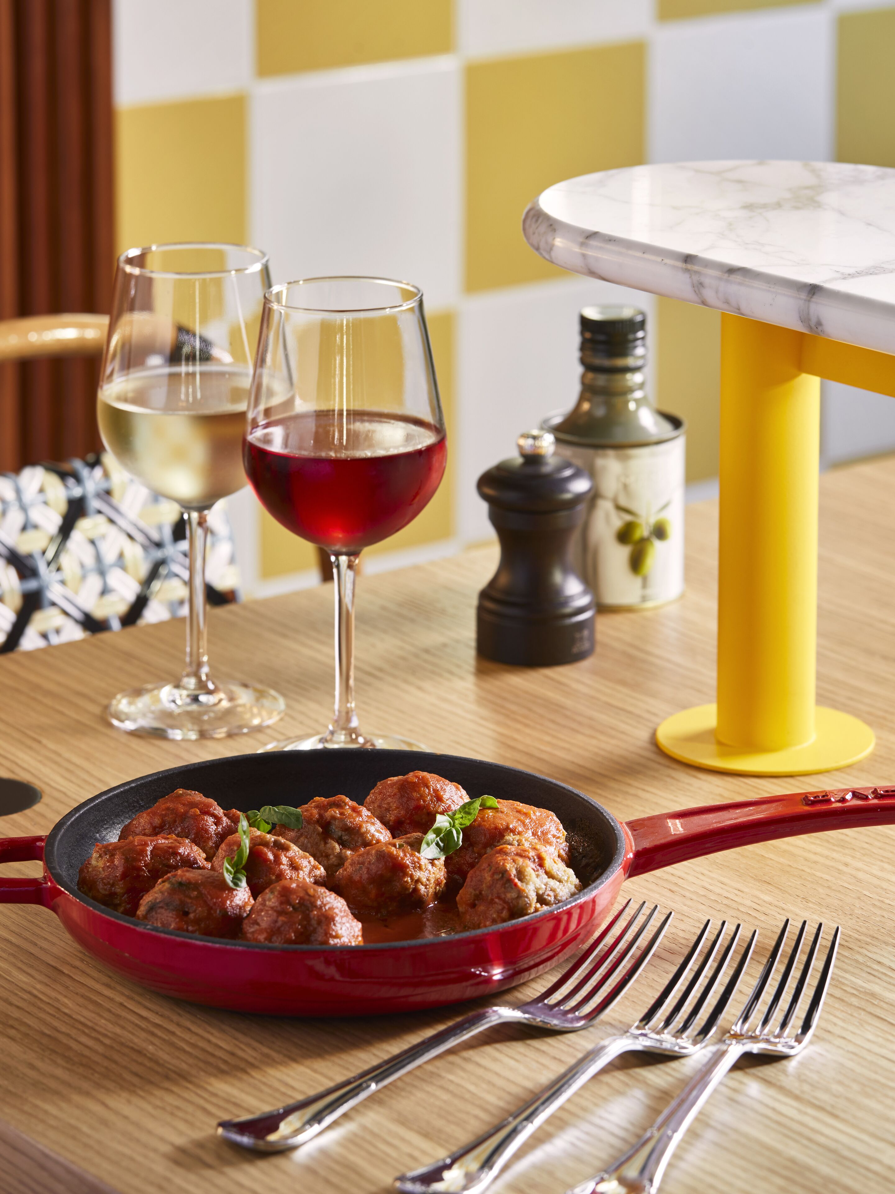 A dining table with a red pan of meatballs, two wine glasses, and a yellow table base.