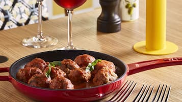 A dining table with a red pan of meatballs, two wine glasses, and a yellow table base.