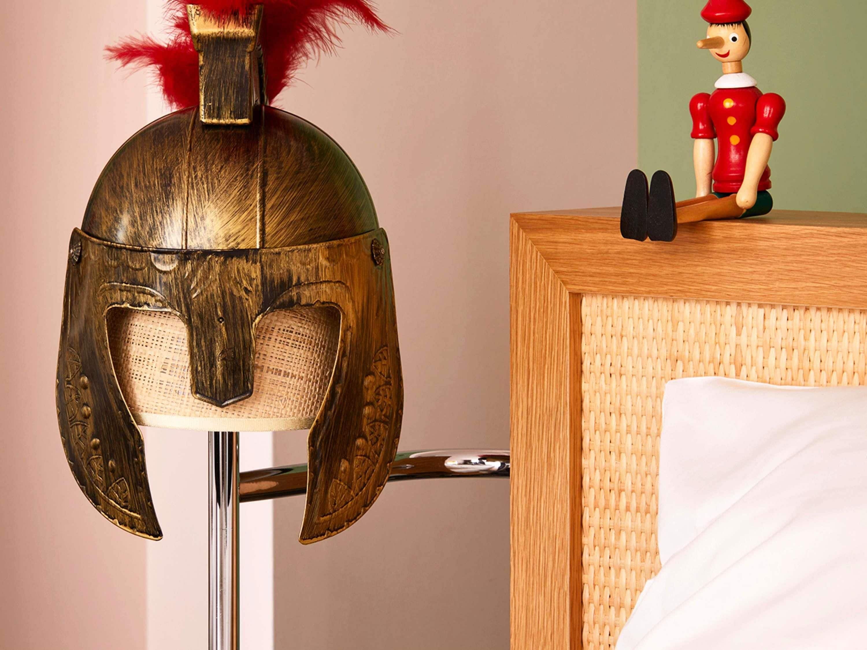 A wooden helmet with a red feather on top, a small figurine, and a wicker basket on a wooden surface.