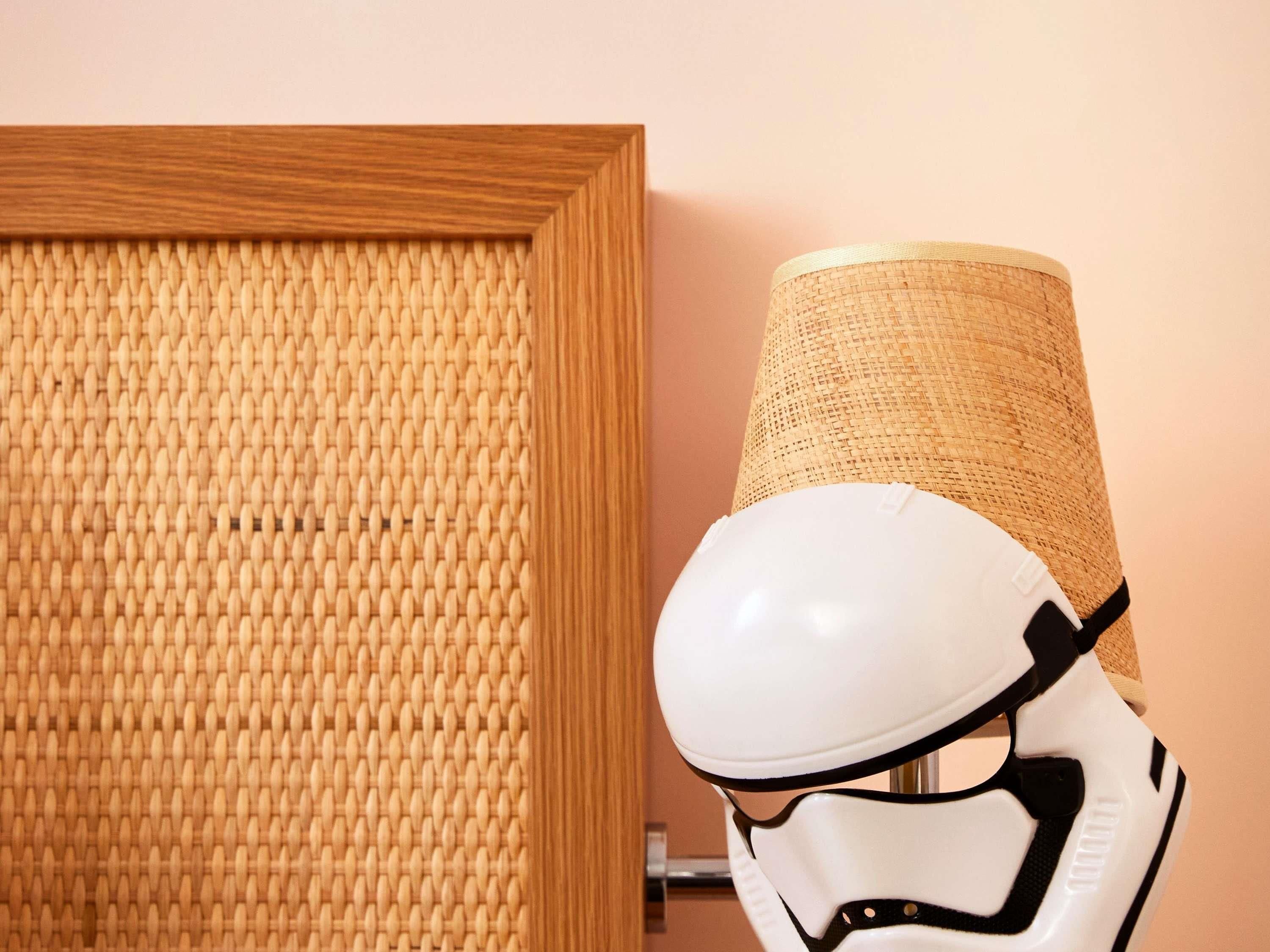 Een kamer met een geweven wandpaneel, een witte helm en een cilindrische rieten lamp.