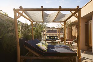 Zona relax esterna e luminosa con un gazebo in legno, sedute imbottite e vista sul giardino e sugli edifici circostanti.
