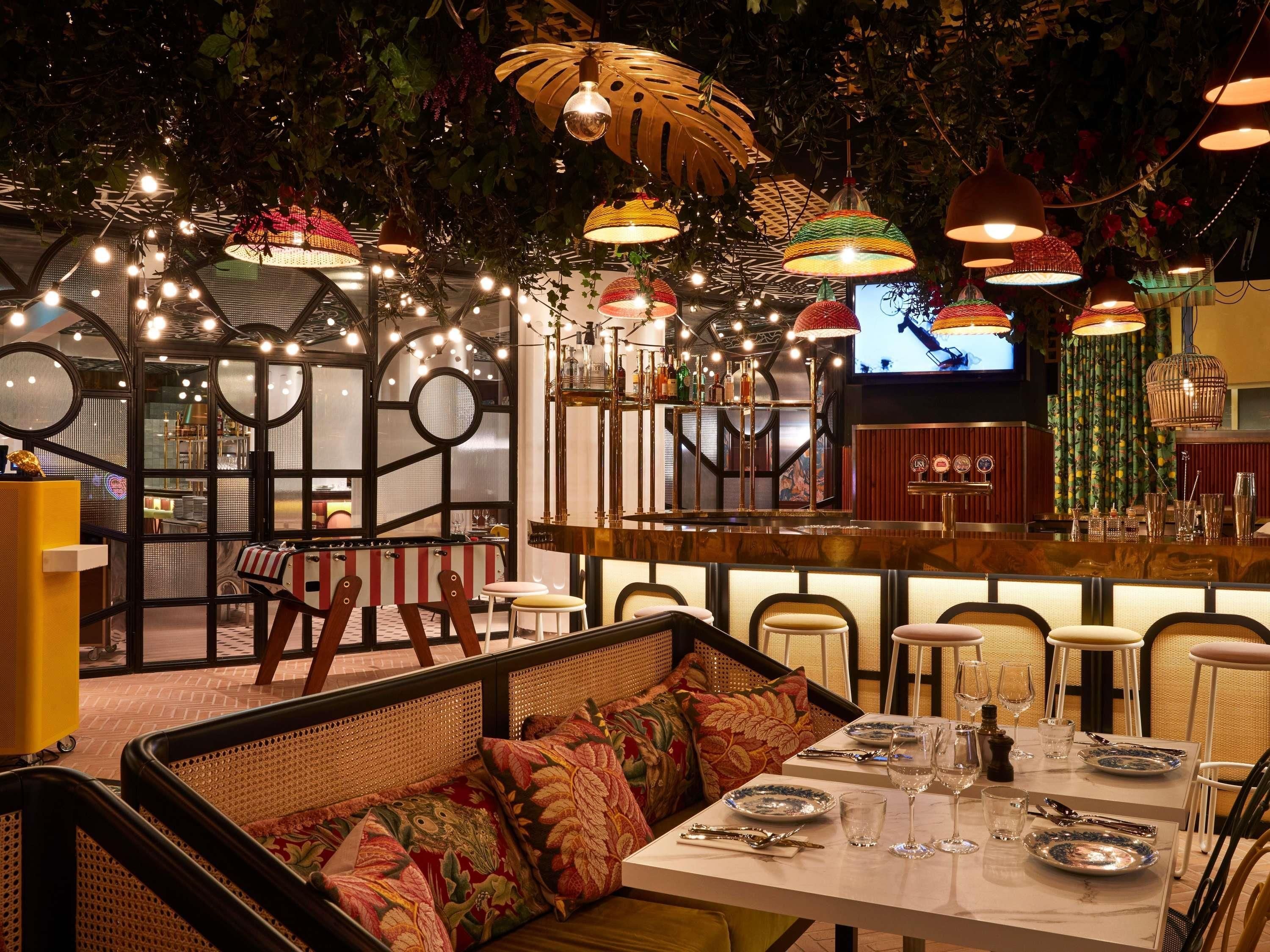 A restaurant with a bar area, wicker furniture, and hanging lamps.