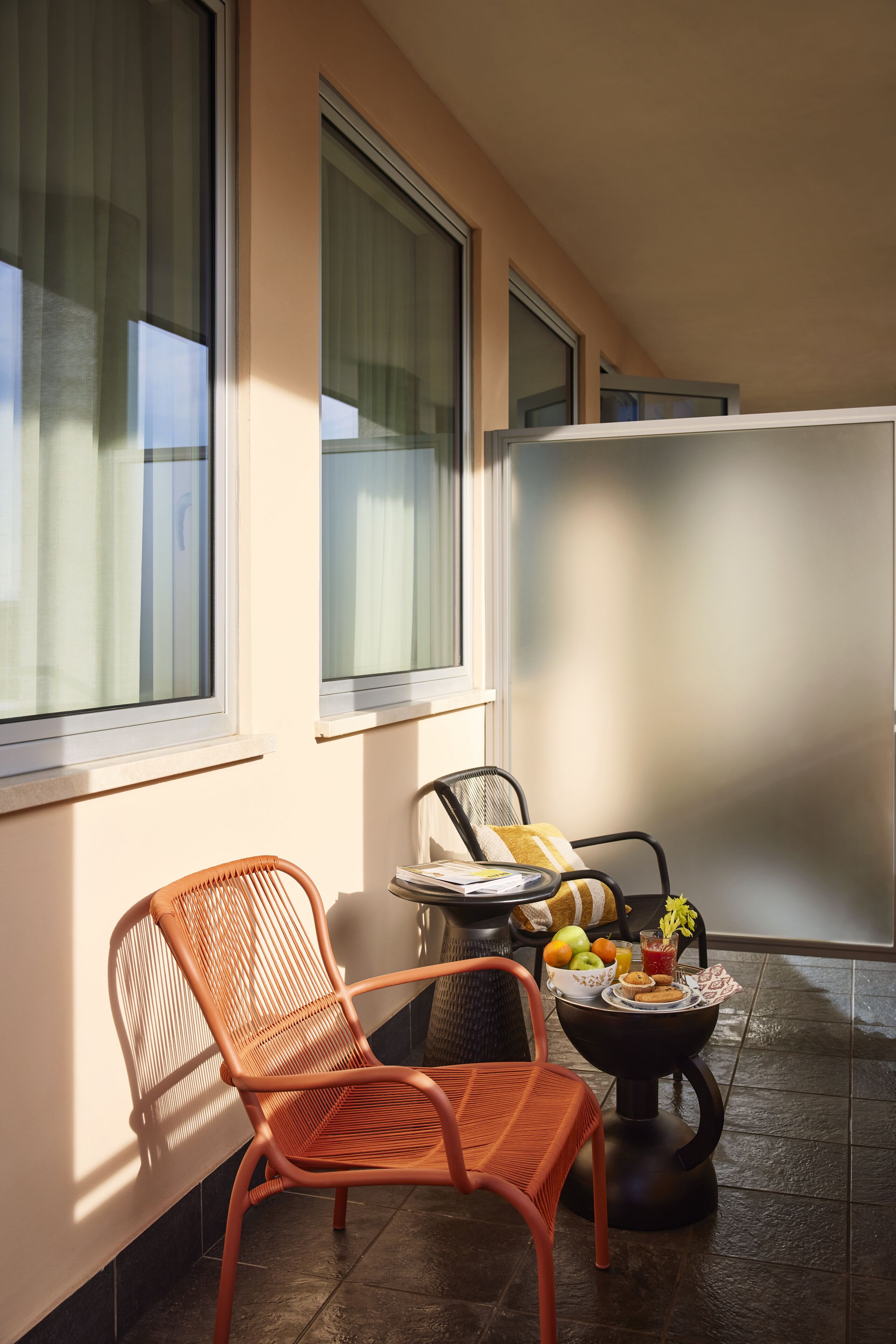 Un balcone con sedie in vimini, un tavolino con frutta e un vaso, e ampie finestre.