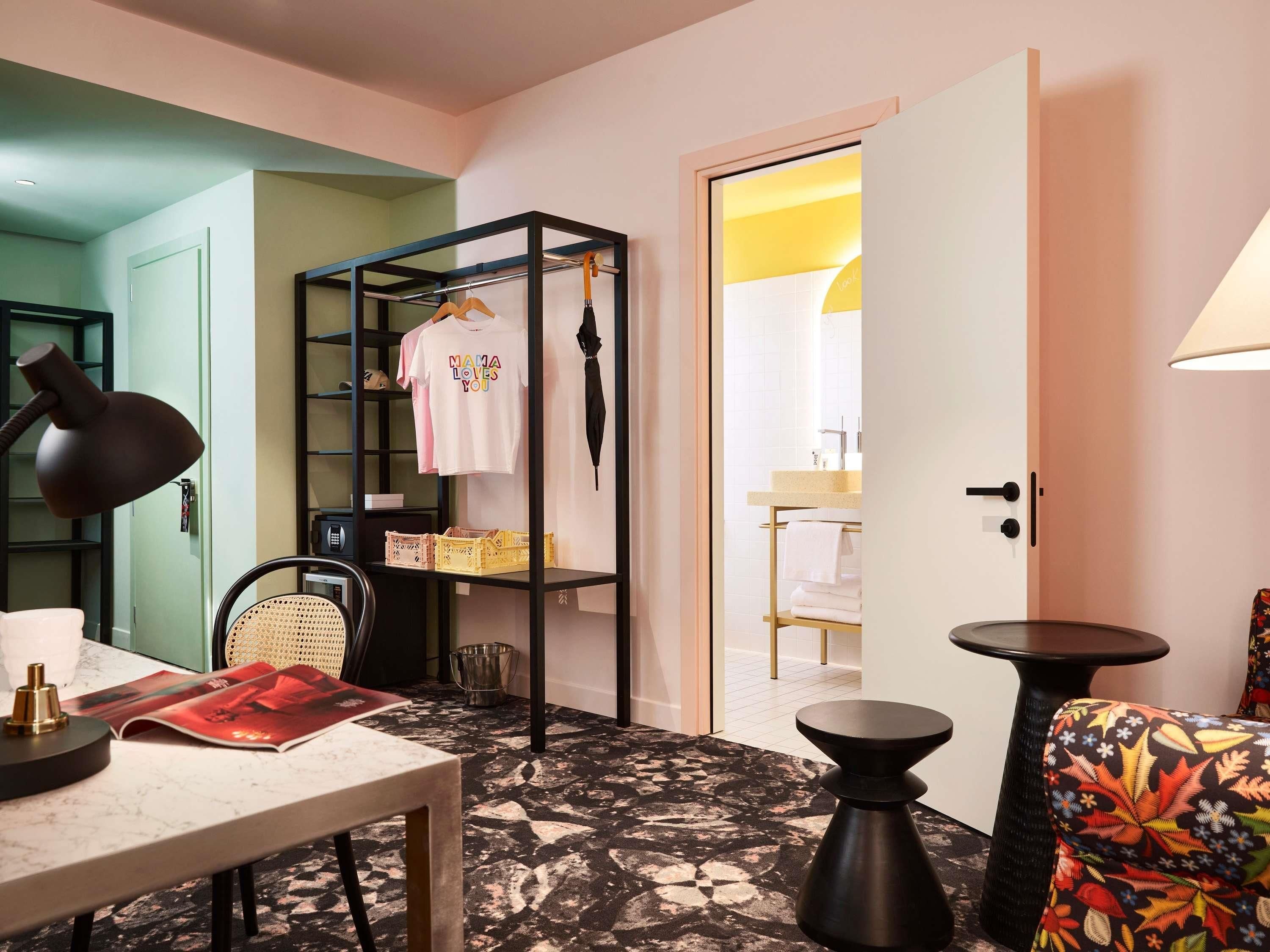 A room with a bed, a desk with a lamp, a chair, a wardrobe, and a bathroom visible through an open door.