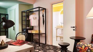 A room with a bed, a desk with a lamp, a chair, a wardrobe, and a bathroom visible through an open door.