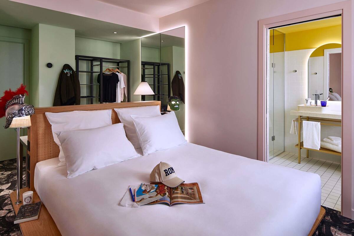 A hotel room with a bed, a mirror, a bathroom with a sink, and a door leading to another room.