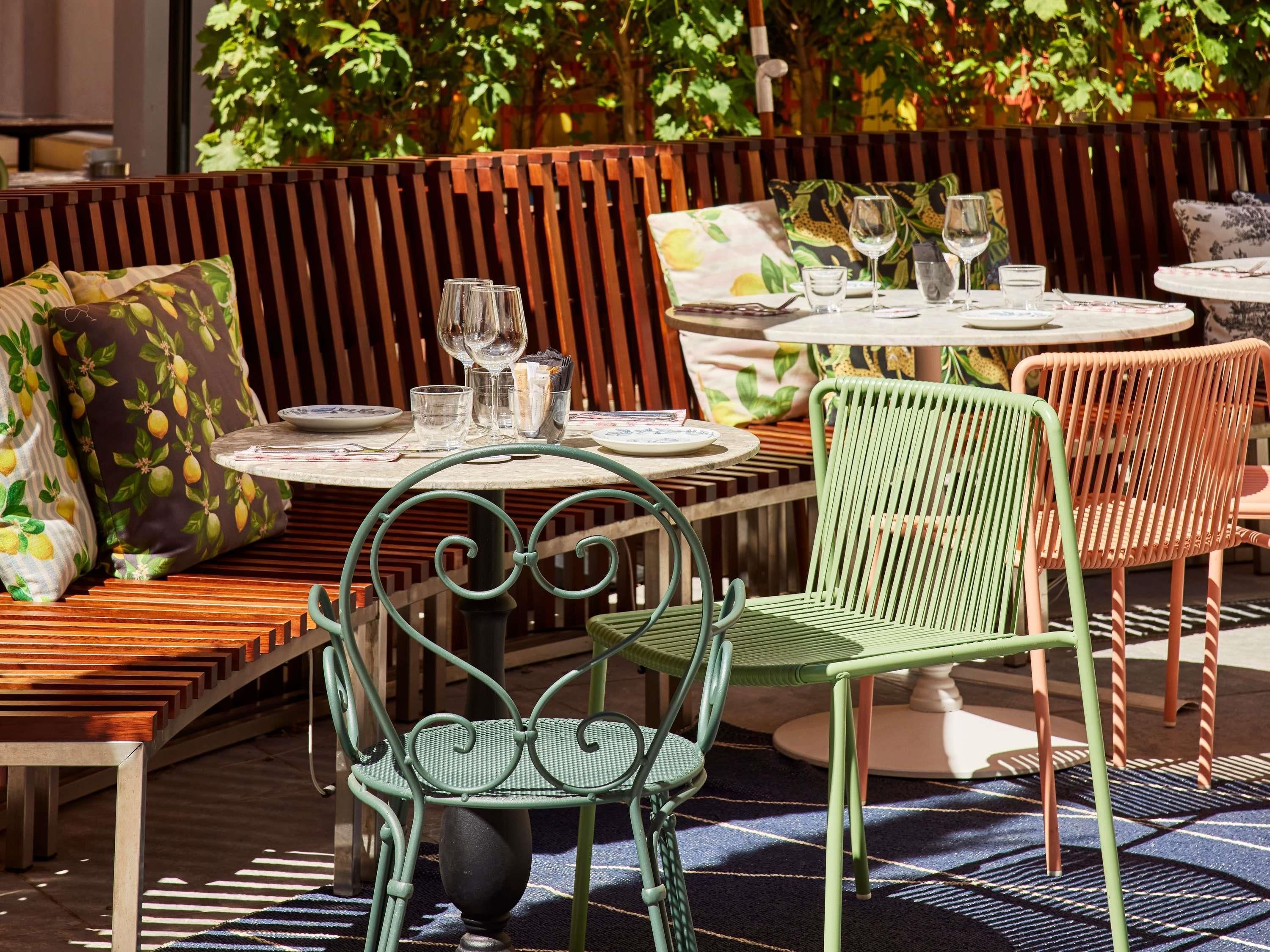 An outdoor seating area with green metal chairs, wooden benches, and tables set for dining.
