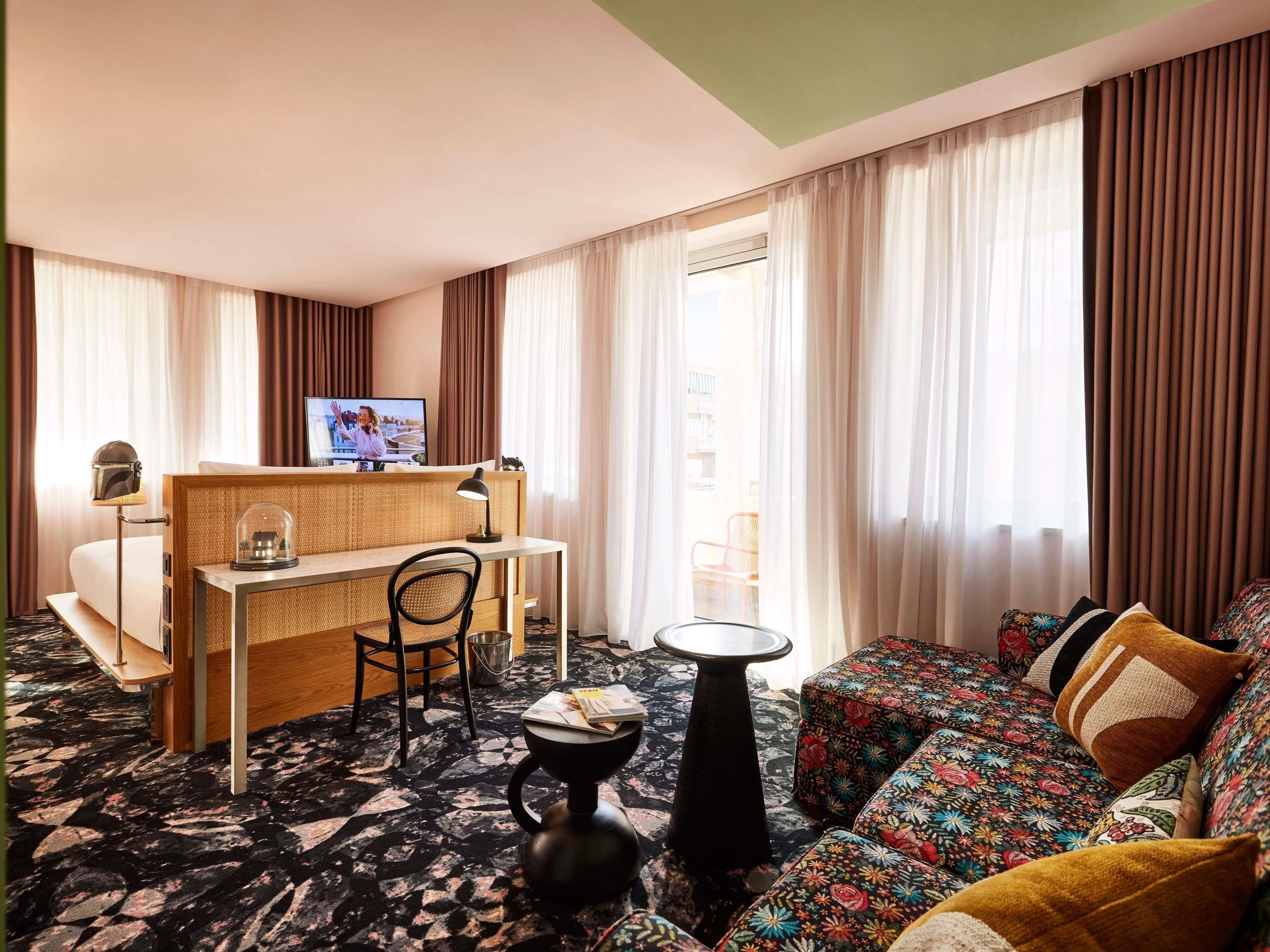 A hotel room with a bed, a desk with a chair, a small table, and a sofa.
