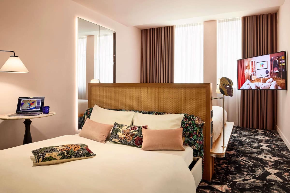 A hotel room with a bed, a TV, a lamp, and a small table with a laptop and glasses.