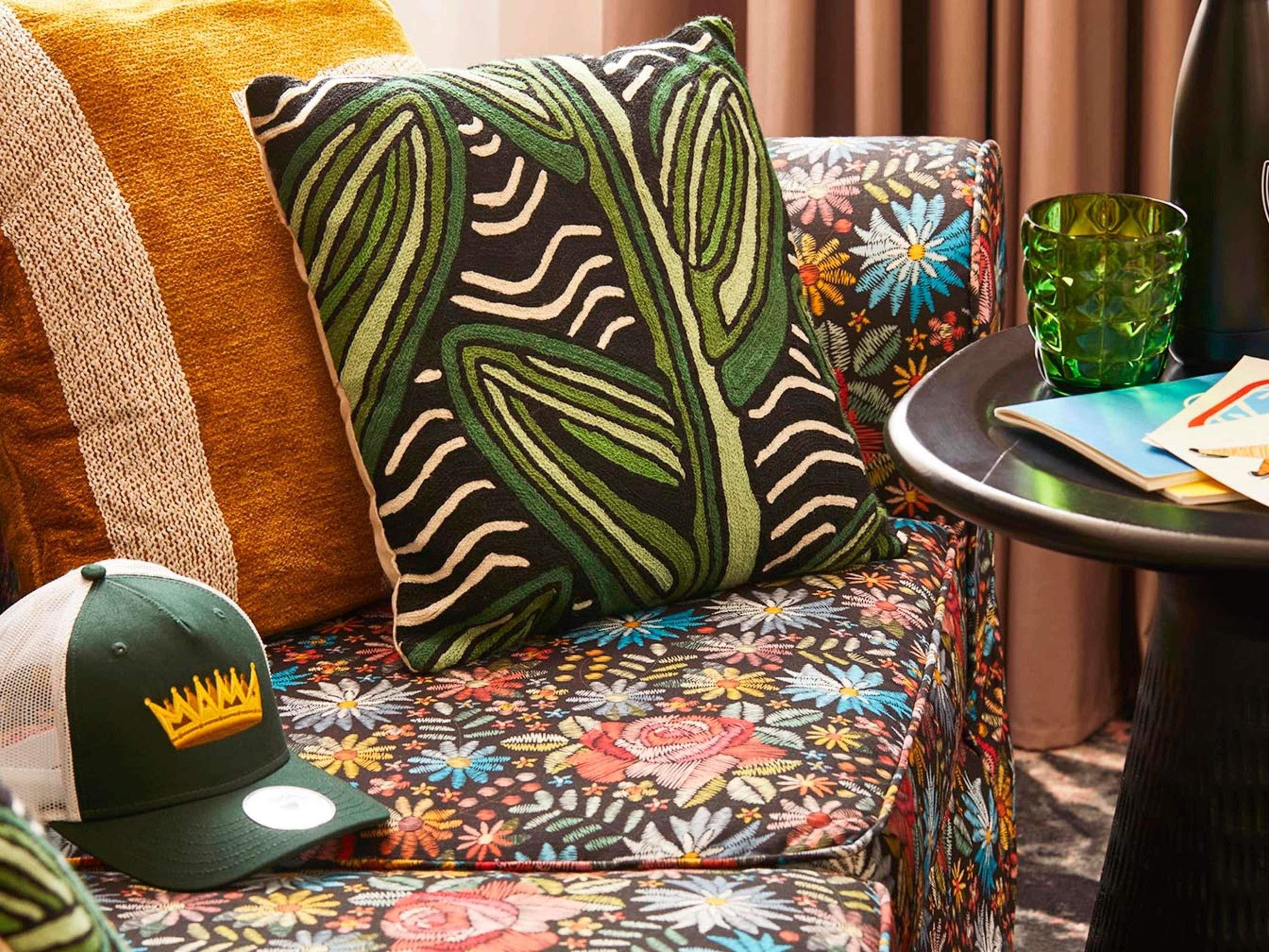Ein Sofa mit einem Blumenmuster, eine grüne und weiße Baseballkappe und ein grünes Glas auf einem Beistelltisch.