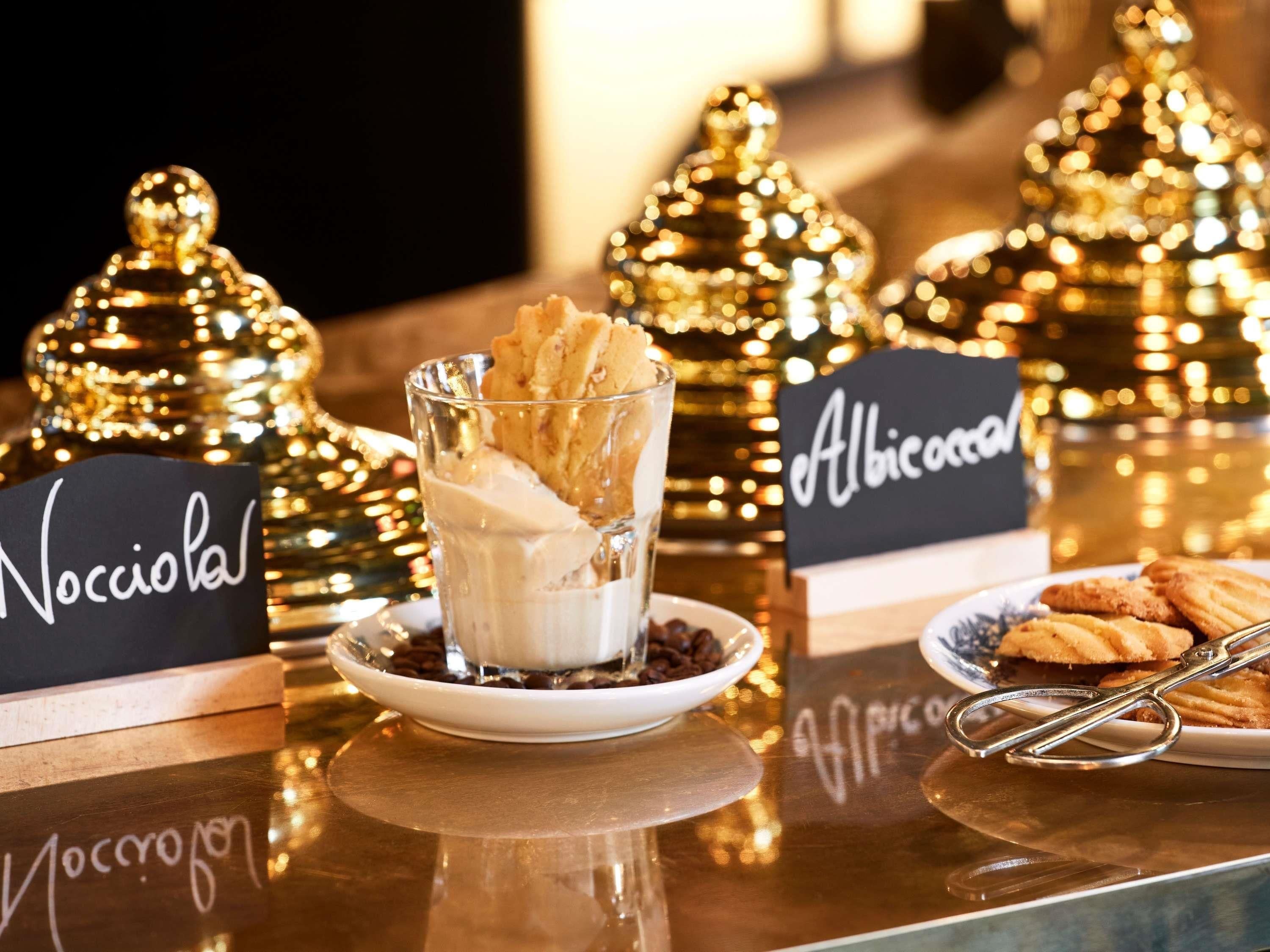 Una zona de postres amb un got de gelat i galetes, amb les etiquetes 'Nocciola' i 'Albicocca', i ornaments daurats decoratius al fons.