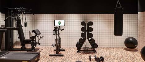 A gym with exercise equipment, a punching bag, and a digital screen.