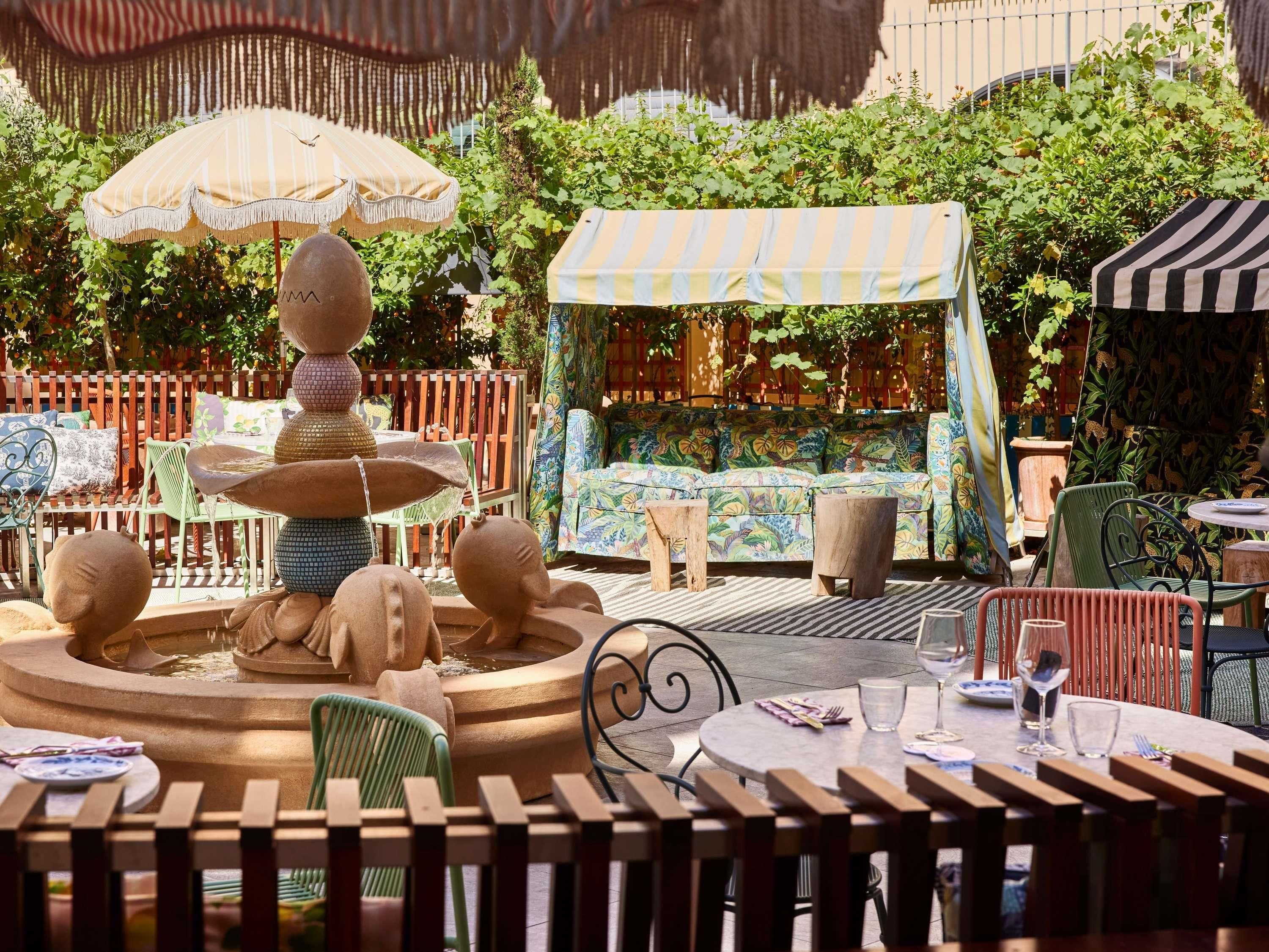 A garden patio with a tiered water fountain, outdoor seating, and umbrellas.