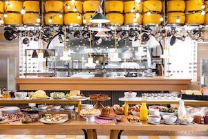 A buffet with various food items and a kitchen area in the background.