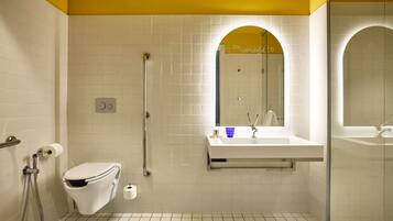 A modern bathroom with a white toilet, a glass shower enclosure, a white sink with a mirror, and a yellow accent wall.