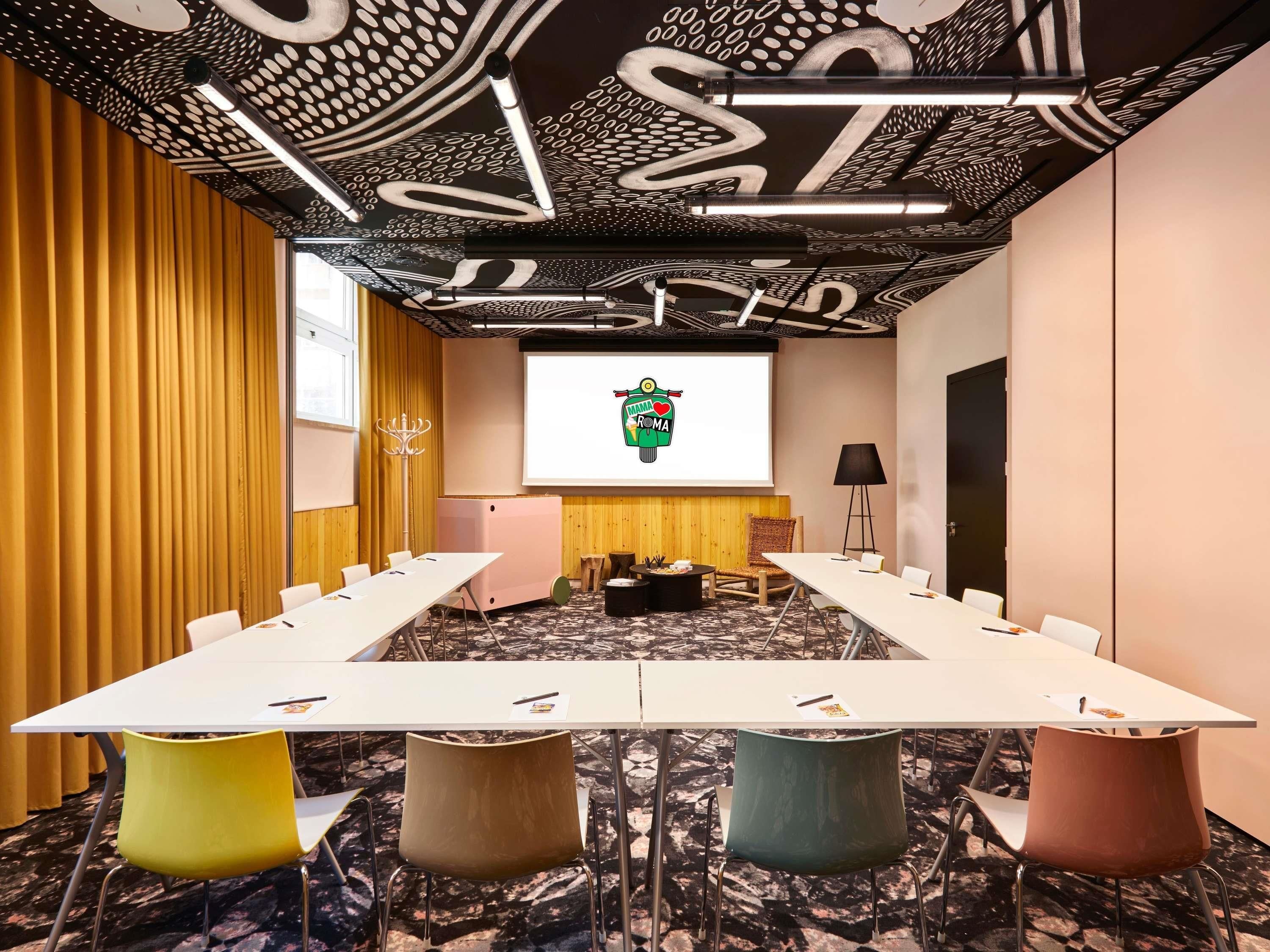 Une salle de conférence avec une longue table, des chaises, un écran de projection et un plafond orné de motifs.