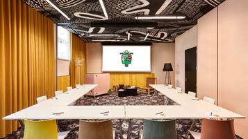 A conference room with a long table, chairs, a projector screen, and a patterned ceiling.