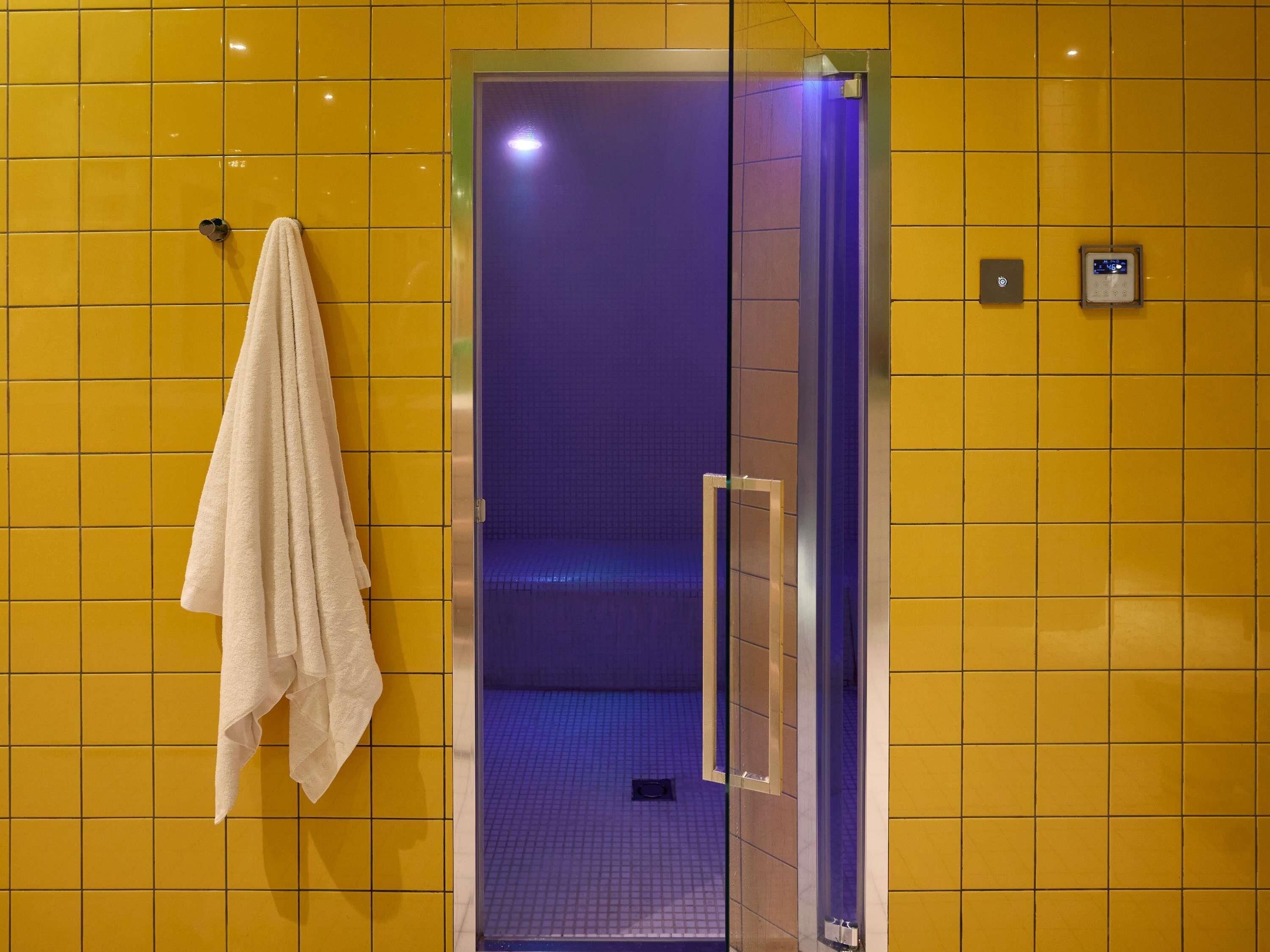 Une salle de bain avec des carreaux jaunes, une douche en verre et une serviette accrochée au mur.