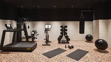 Une salle de sport équipée d’un tapis de course, d’un vélo elliptique, d’un vélo d’appartement, d’un banc de musculation, d’haltères et de ballons d’exercice.