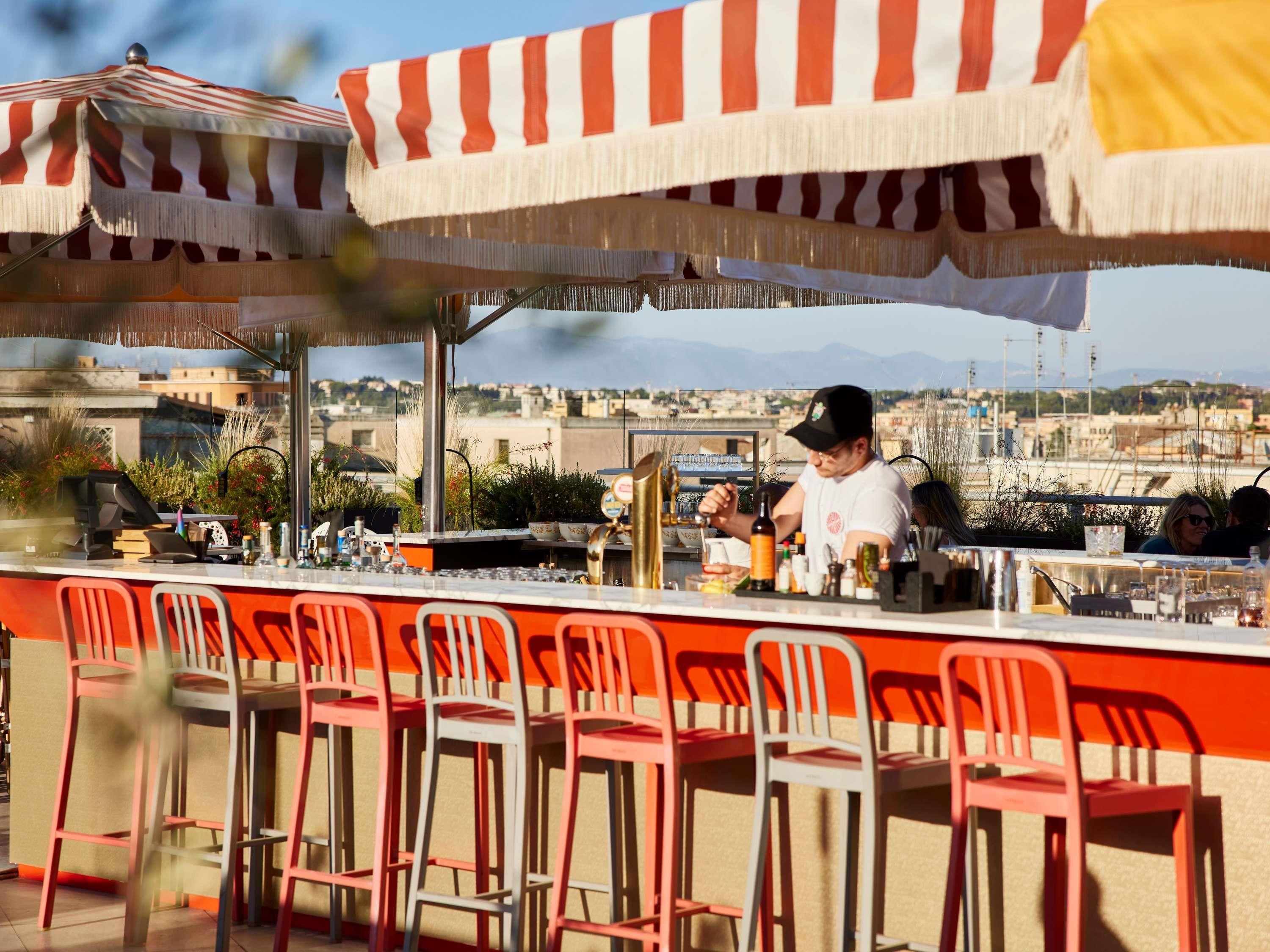 A bar area with a bartender, outdoor seating, and a view of the cityscape.