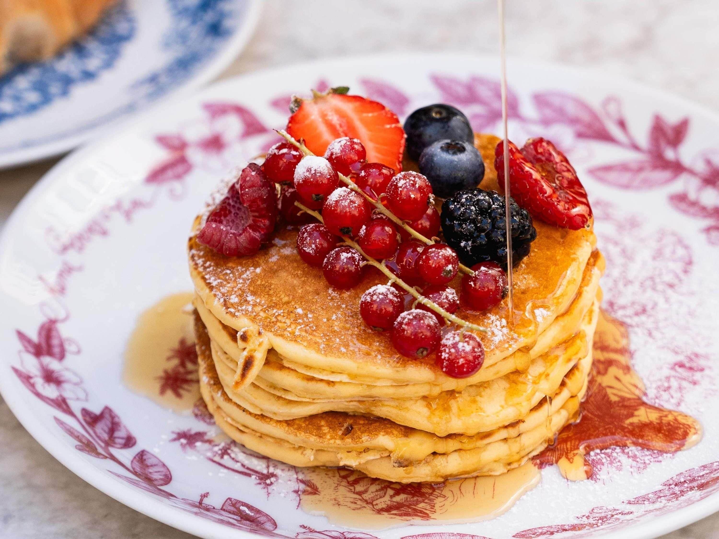 A stack of pancakes with berries and syrup on a floral plate.