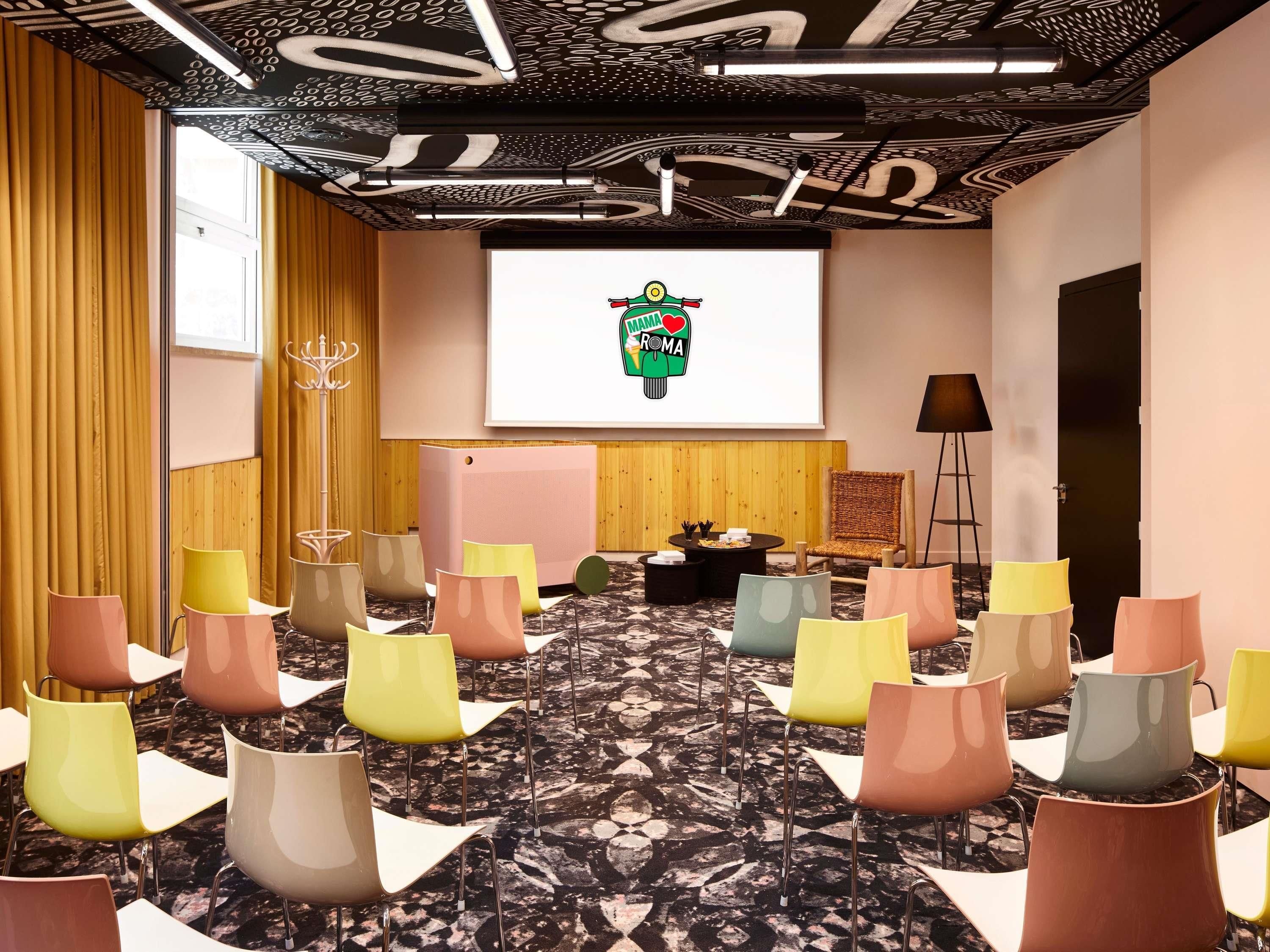 A conference room with a projector screen, multiple chairs, a wooden panel wall, and a patterned carpet.
