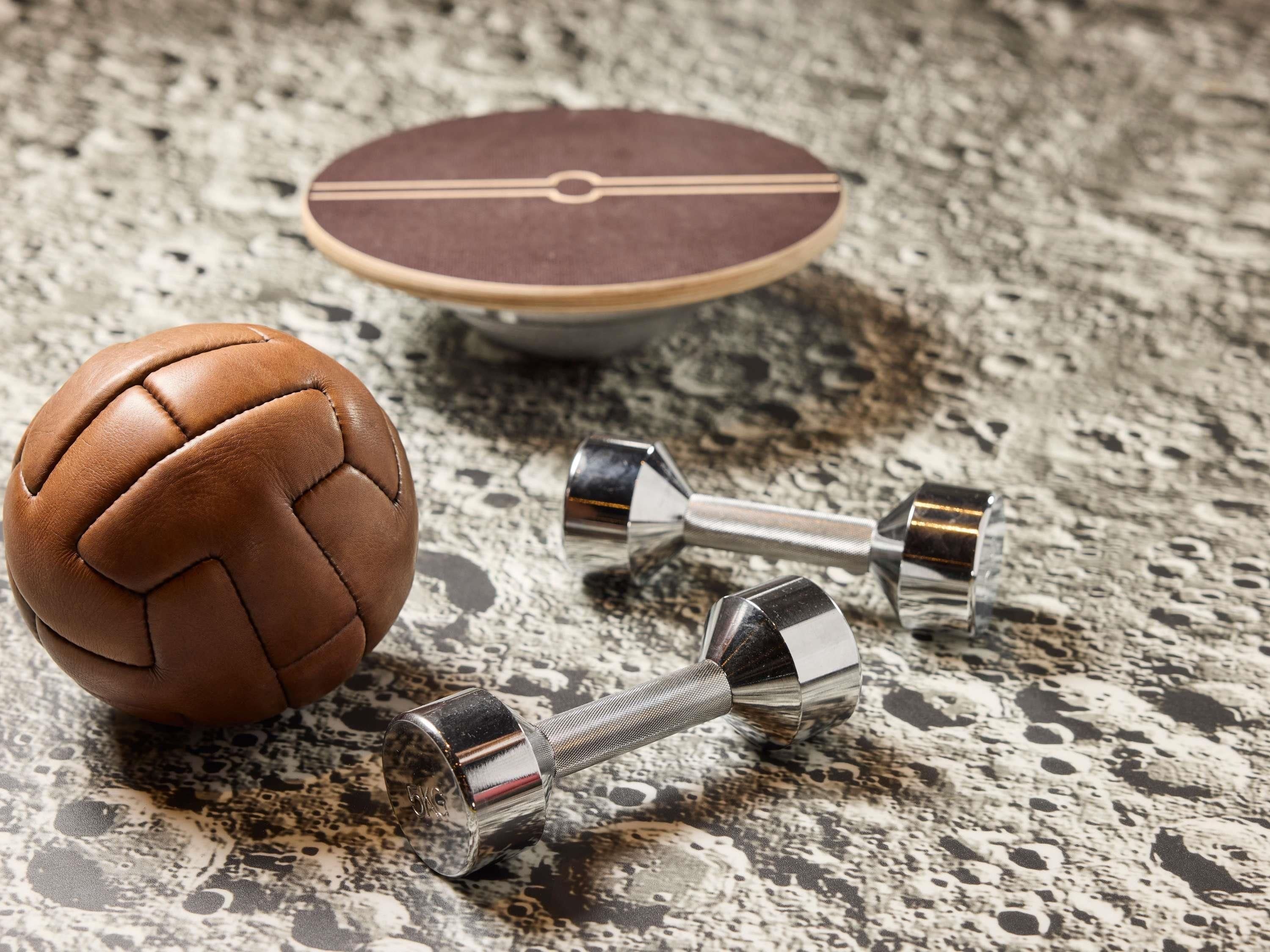 A brown leather ball and two metallic dumbbells on a textured surface.