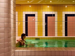 A woman sitting by a pool with tiled walls in a geometric pattern. - Mama Shelter Roma  (Rome)