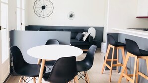 Un espace de vie moderne avec une table ronde blanche, des chaises noires, un canapé gris foncé et un élément décoratif géométrique sur le mur.